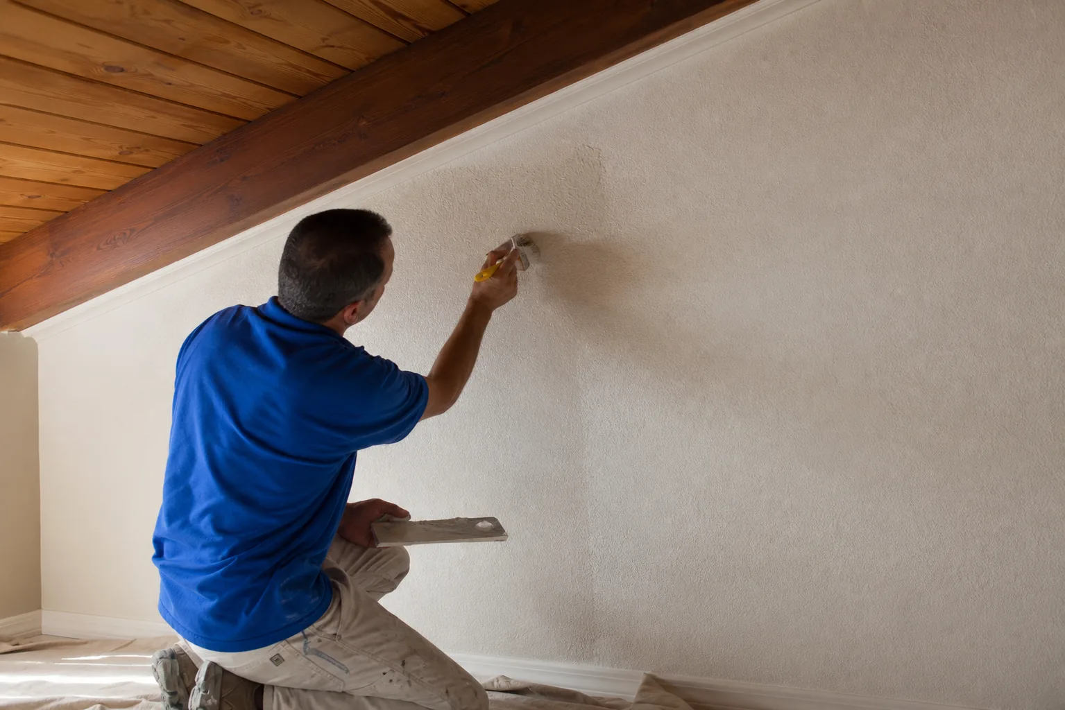 Contractor hand-applying a subtle matching texture near a ceiling and wall junction